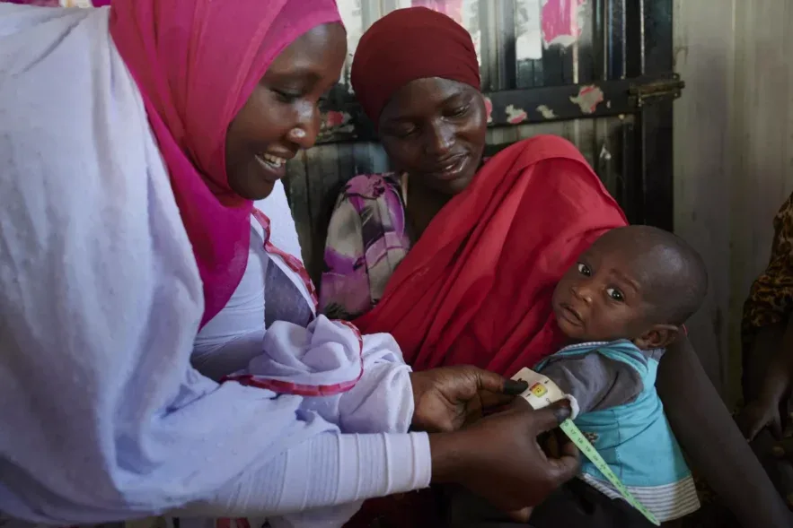 طفل سوداني يجلس أمام خيمة في أحد مخيمات النزوح بإقليم دارفور، وإلى جانبه والدته تحمل وعاءً من المياه، في مشهد يعكس معاناة الأطفال من سوء التغذية ونقص المياه الآمنة في منطقة جبل مرة.