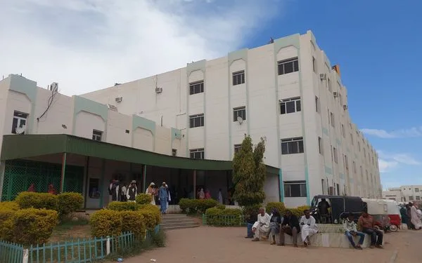 مدخل مستشفى دنقلا التخصصي في الولاية الشمالية بالسودان، وبجانبه كوادر طبية بالزي الأبيض، تعبيرًا عن إدانة الاعتداء على الأطباء داخل المنشآت الصحية.